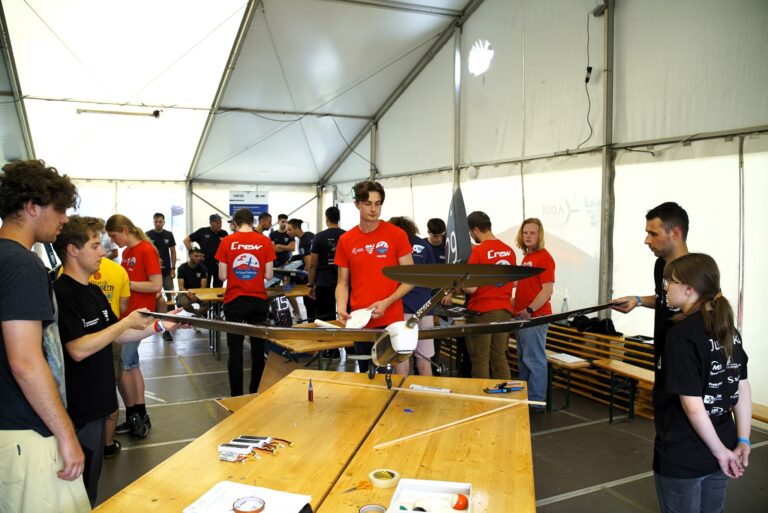 Zdjęcie przedstawia studentów K.N. EUROAVIA Rzeszów, podnoszących model EA-02 Nightlight w celu sprawdzenia położenia środka ciężkości, czy znajduje się on w jednej trzeciej płata na zawodach ACC2024